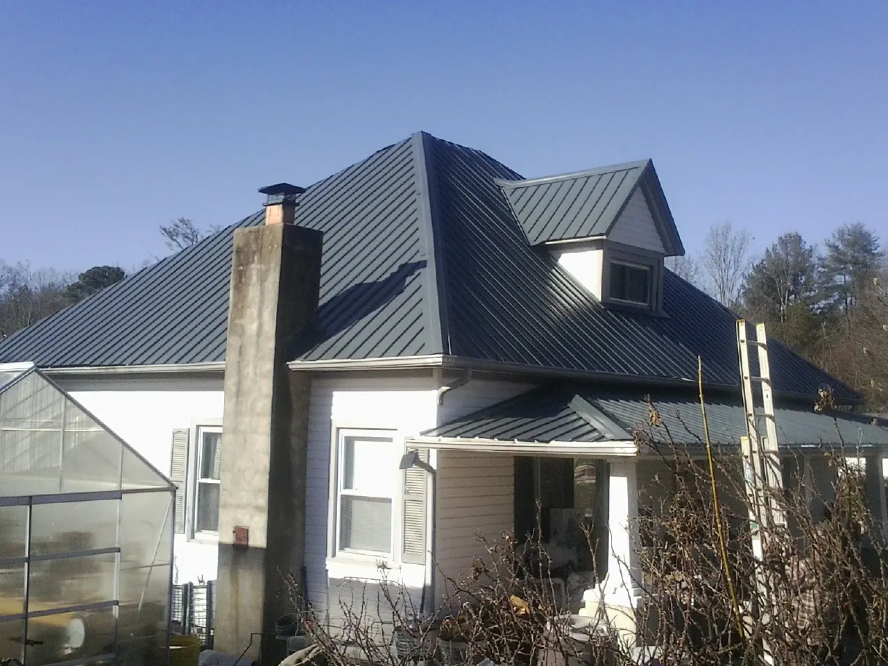Dark blue standing seam metal roof on a white farmhouse with dormer — Slate & Tile Roof Repair by Roofing Brothers in Twin Lake
