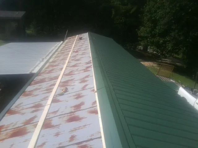 Old rusted panels beside newly installed green metal roofing — Wind Damage Roof Repair by Roofing Brothers in Twin Lake