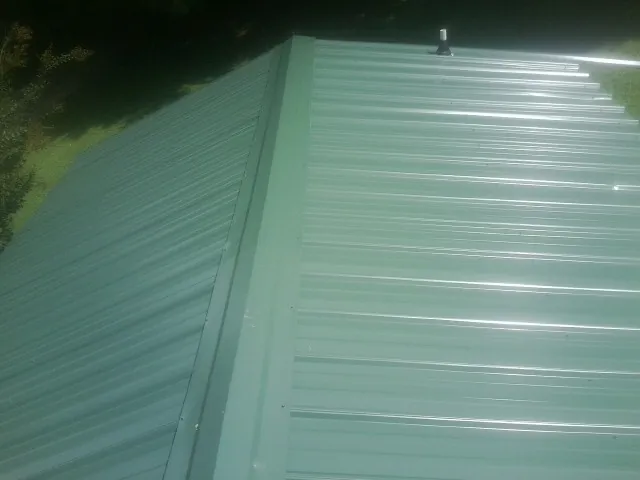 New green metal panels meeting at the ridge of a roof — Flat Roof Repair work by our crew in Twin Lake