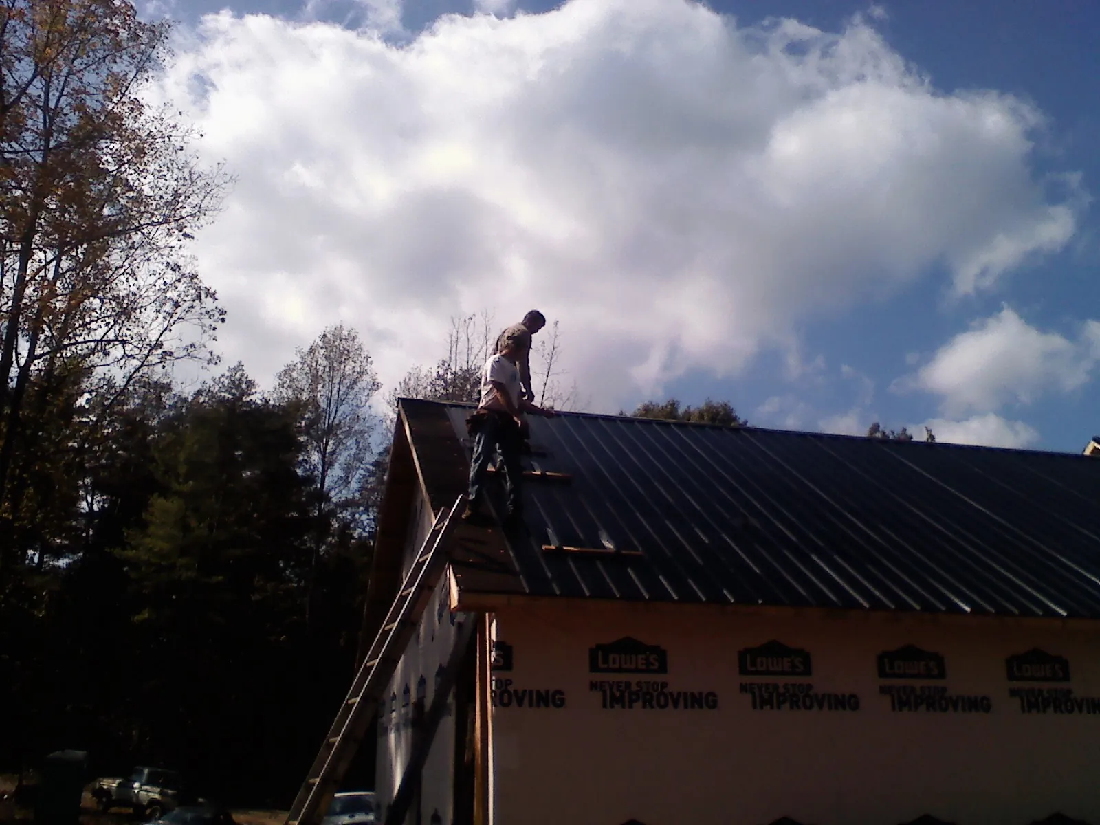 Roofer fastening dark metal panels high against a cloudy sky, from a Roof Inspection job in Twin Lake