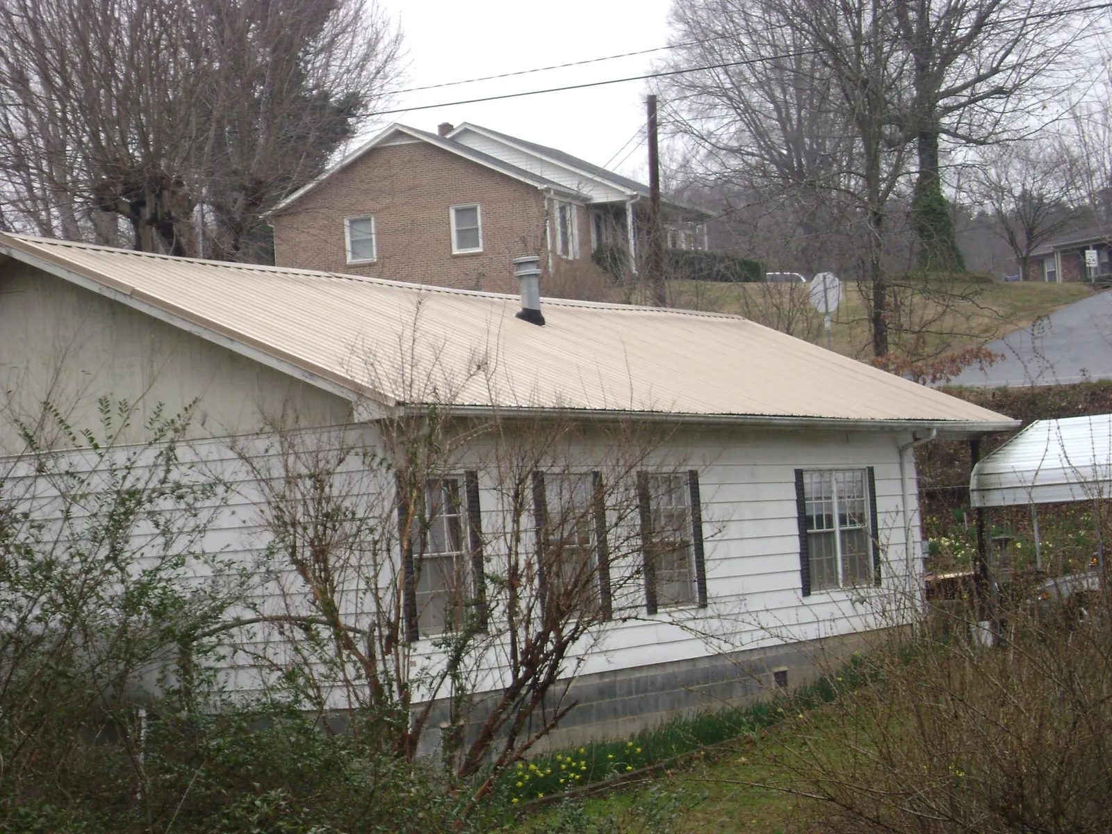 Tan metal roof on a white sided house set into a hillside — Commercial Roofing by Roofing Brothers in Twin Lake